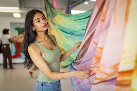 Student looking at and feeling brightly coloured fabrics hanging from the ceiling