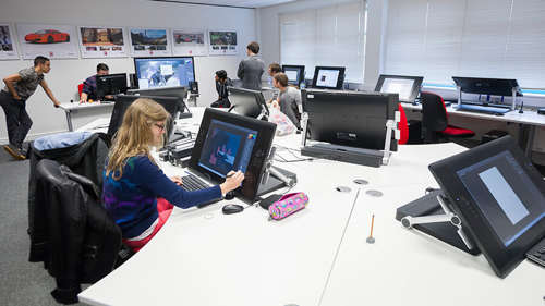 A room full of students working on Game Art designs, with a student in the foreground drawing on a large digital tablet